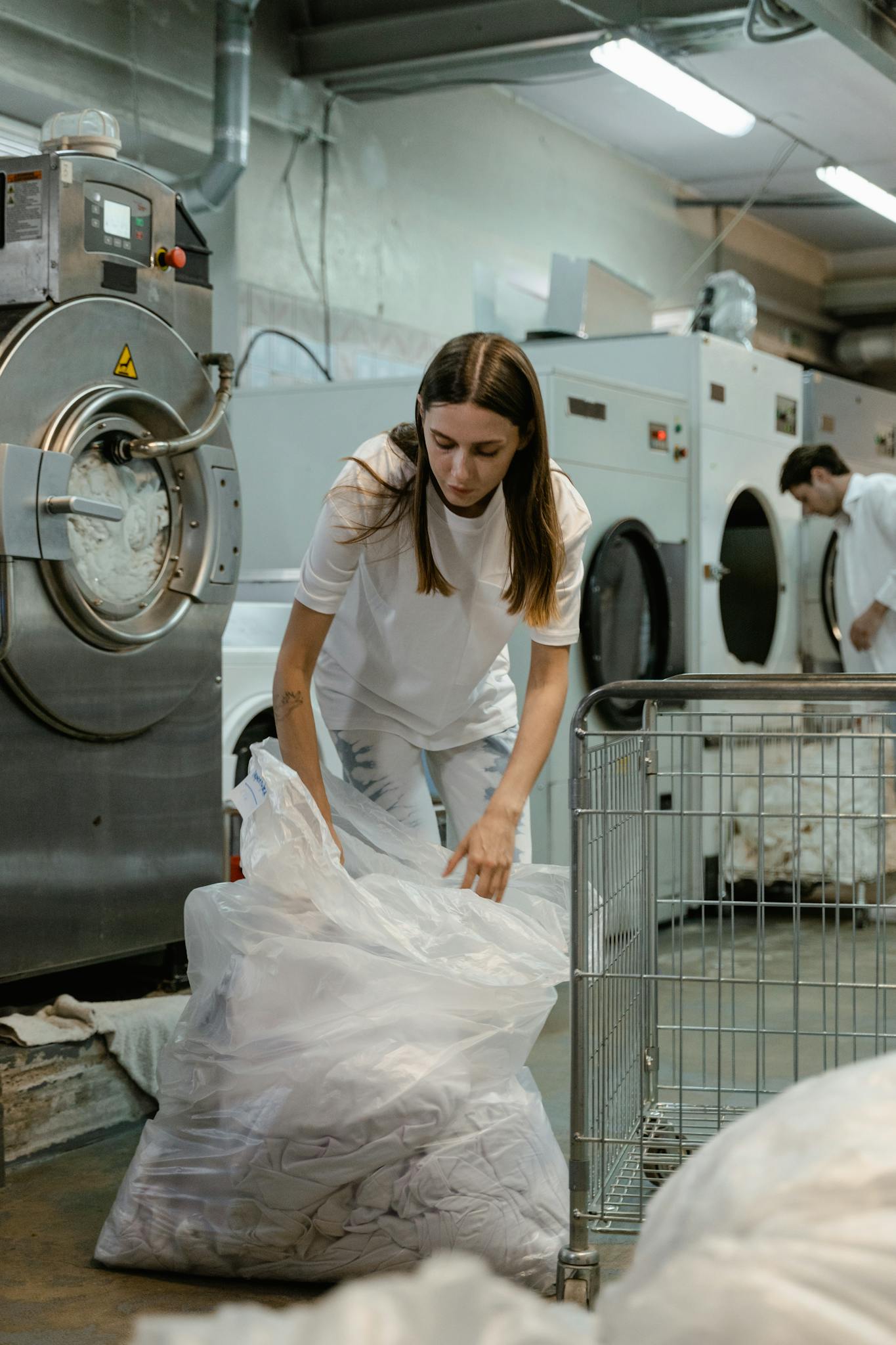 Woman handling laundry in a commercial washing facility, focusing on tasks and efficiency.